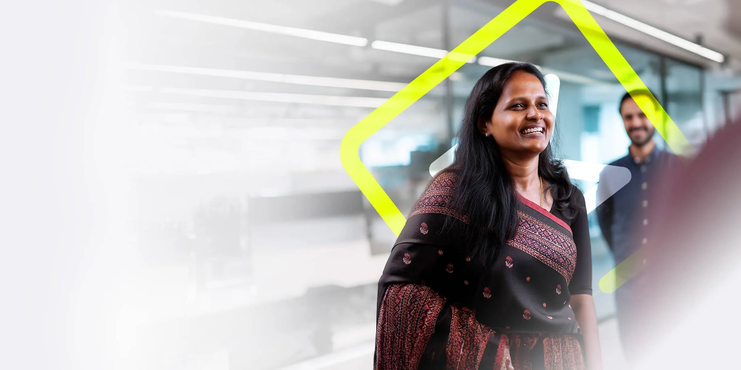 A woman wearing a patterned sari is stood in a modern glass office discussing work with her colleagues