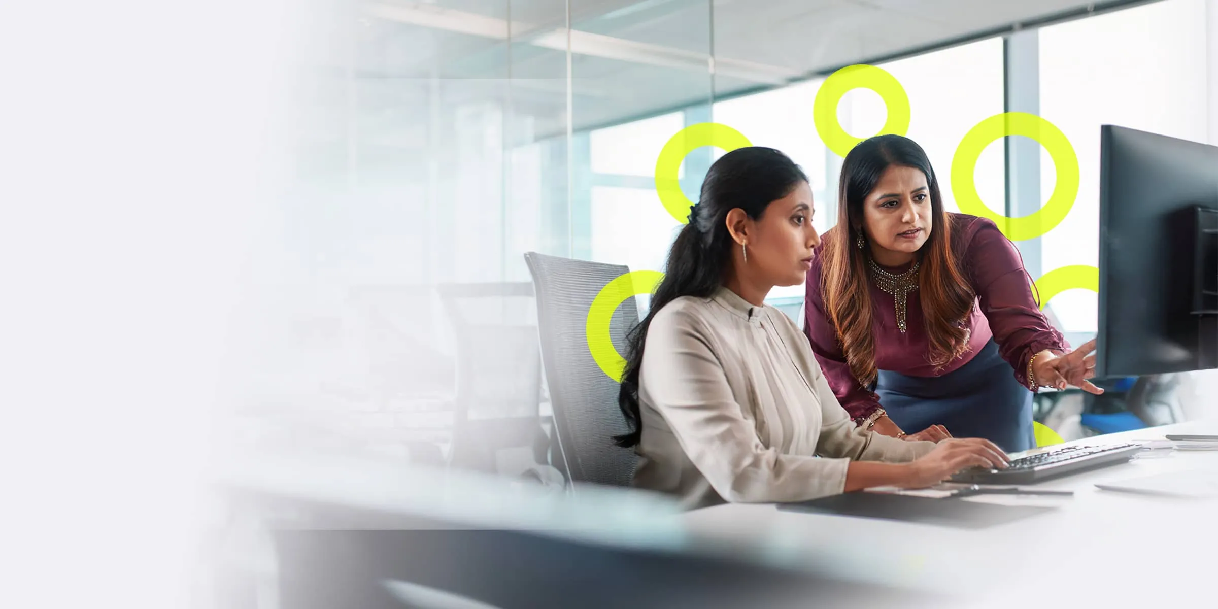 two smartly dressed women discuss work whilst looking at a computer monitor together