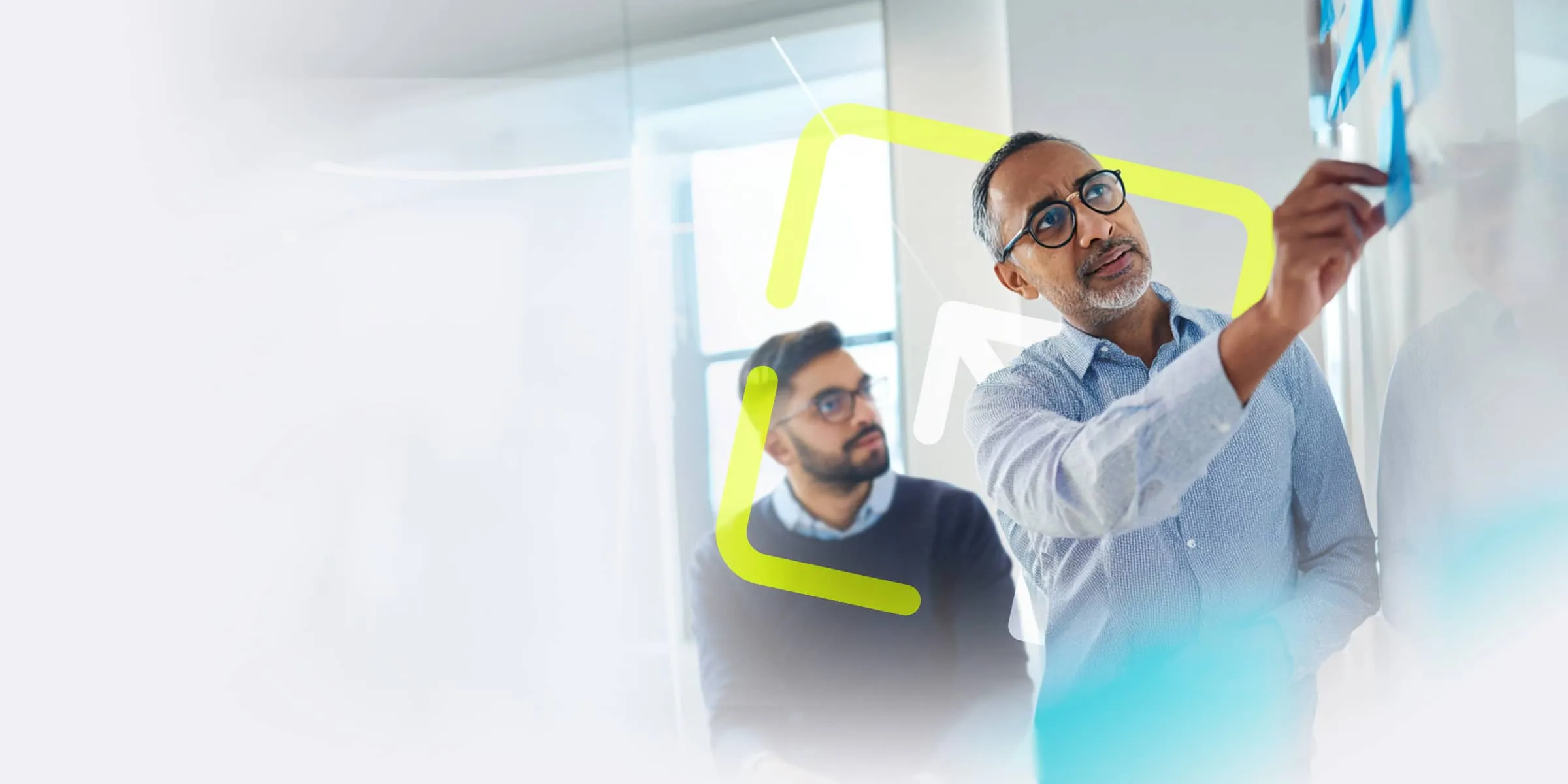 older man with a white beard wearing glasses sticks a blue sticky note to a whiteboard